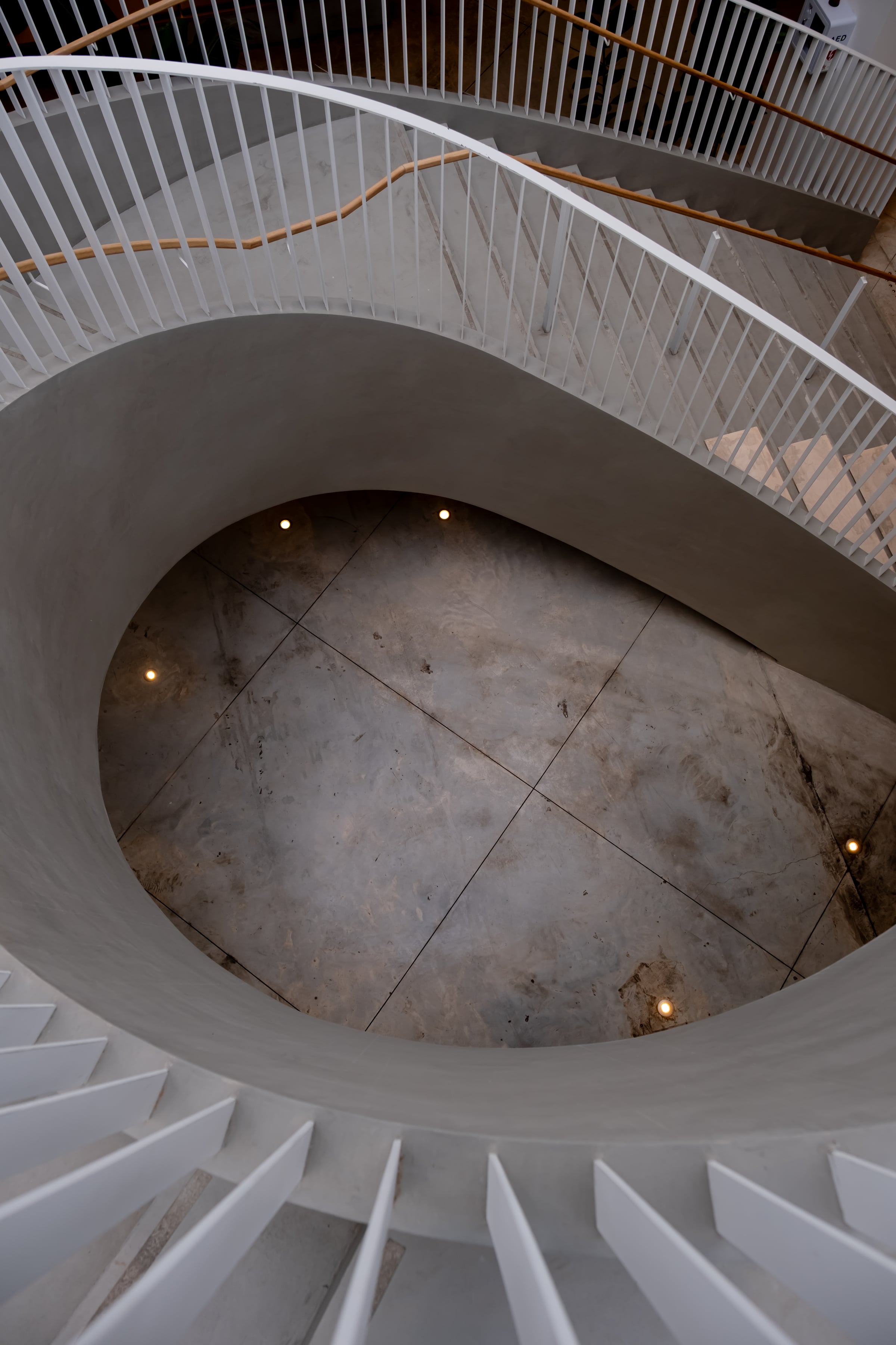 Looking straight down a spiral staircase, oval concrete floor below