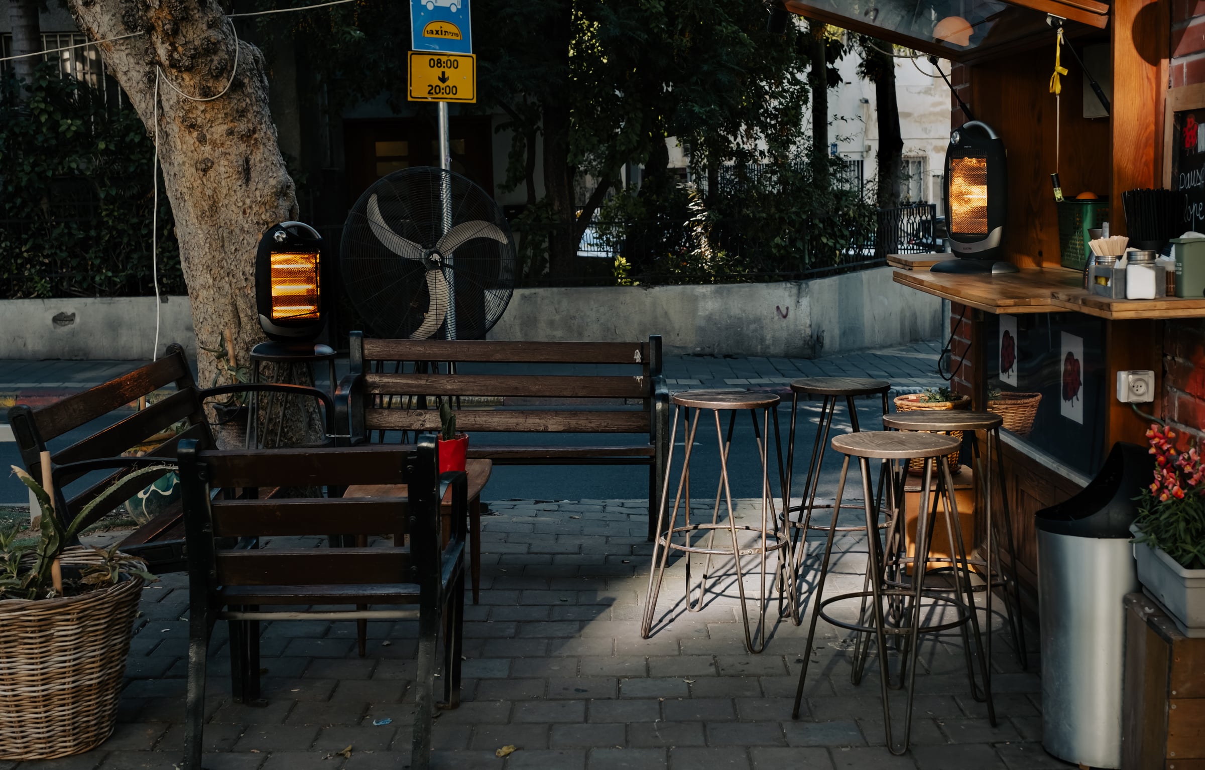 Empty café sidewalk seating with outdoor heaters glowing orange and wooden benches