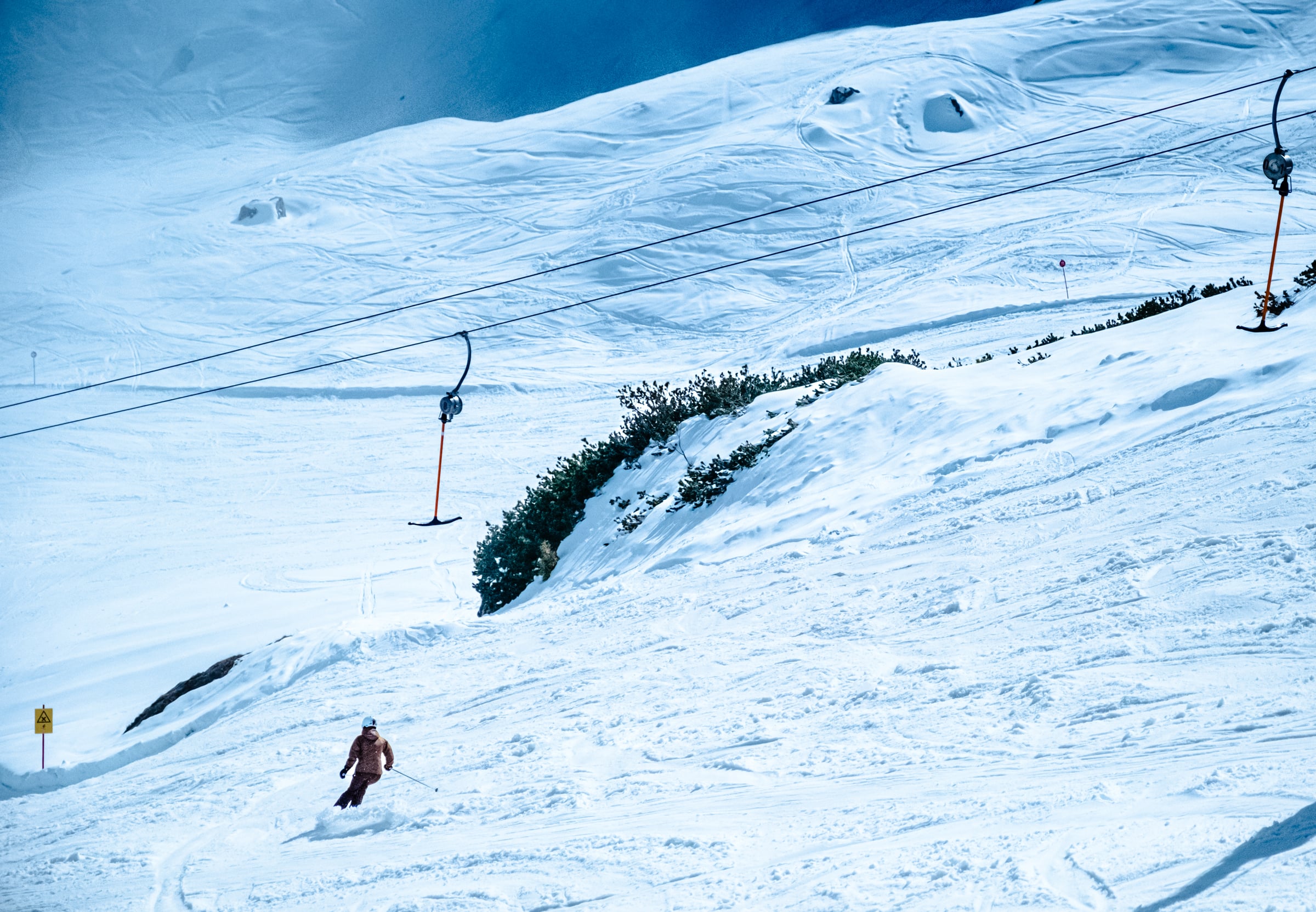 Single skier on pristine snow slope with ski lift cable and electric blue sky