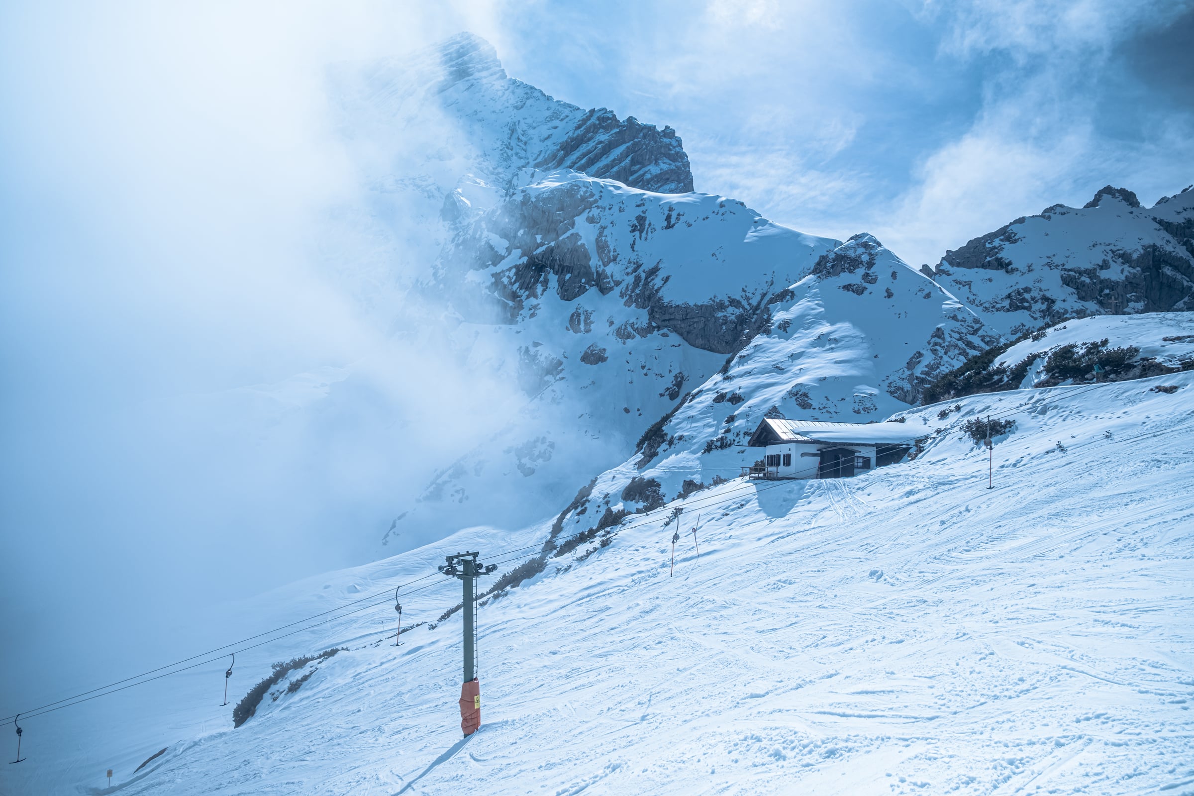 Dramatic alpine mountain peak emerging from fog with ski chalet and lift poles in foreground