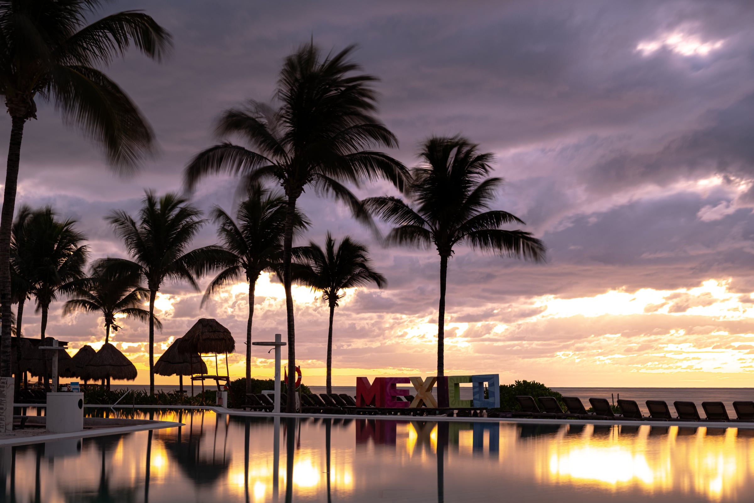 Sunset at Mexican resort pool with MEXICO sign reflected in still water, palm silhouettes