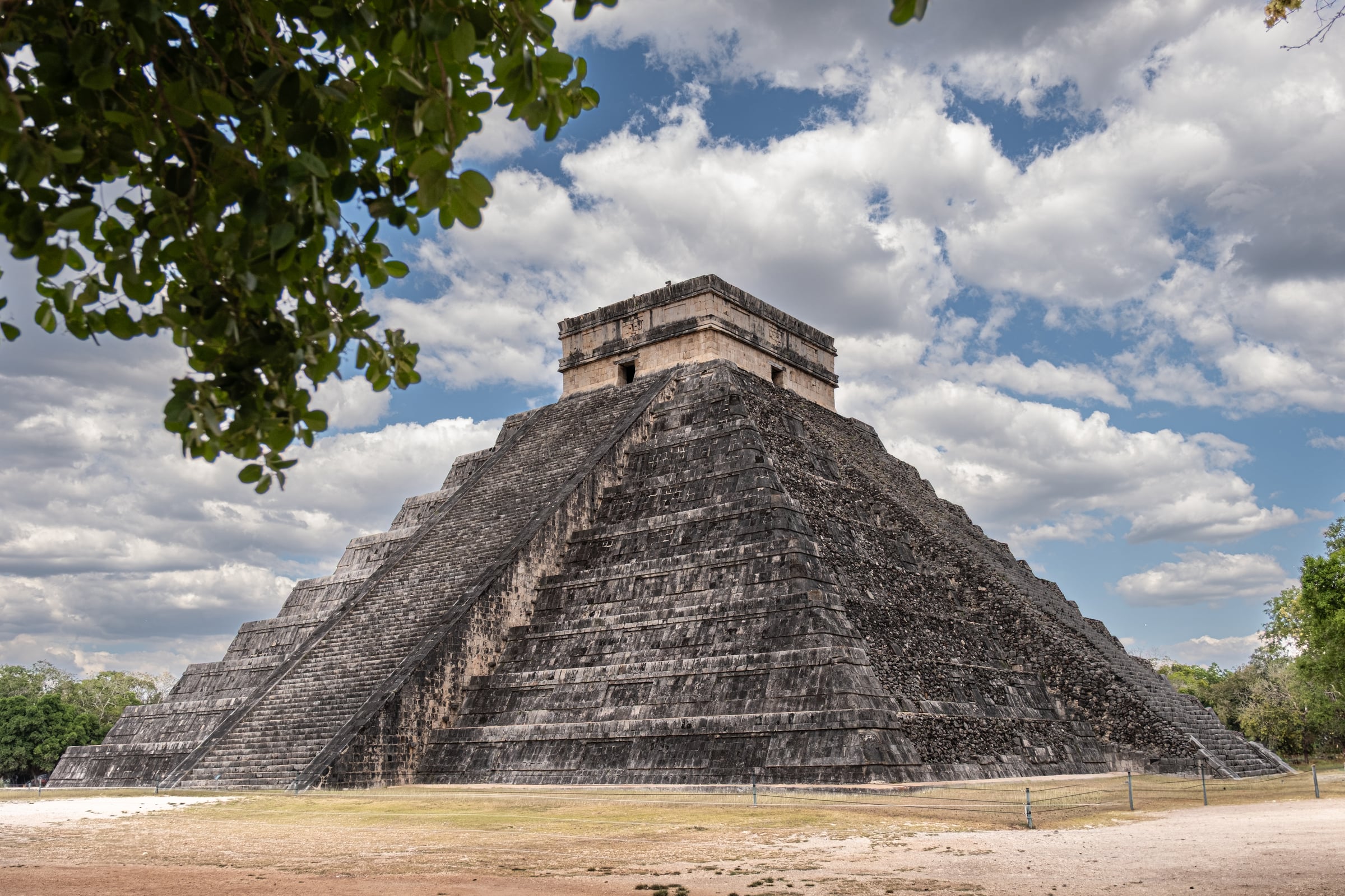 El Castillo pyramid framed by tree branch from a different angle under clouds