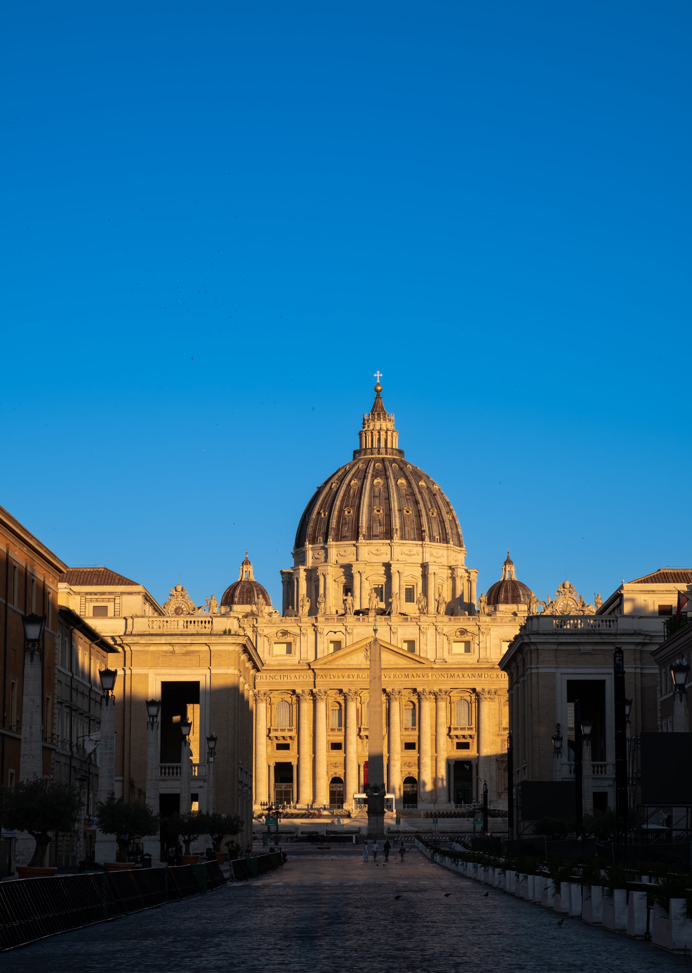 St. Peter's Basilica bathed in golden morning light seen from Via della Conciliazione against deep blue sky