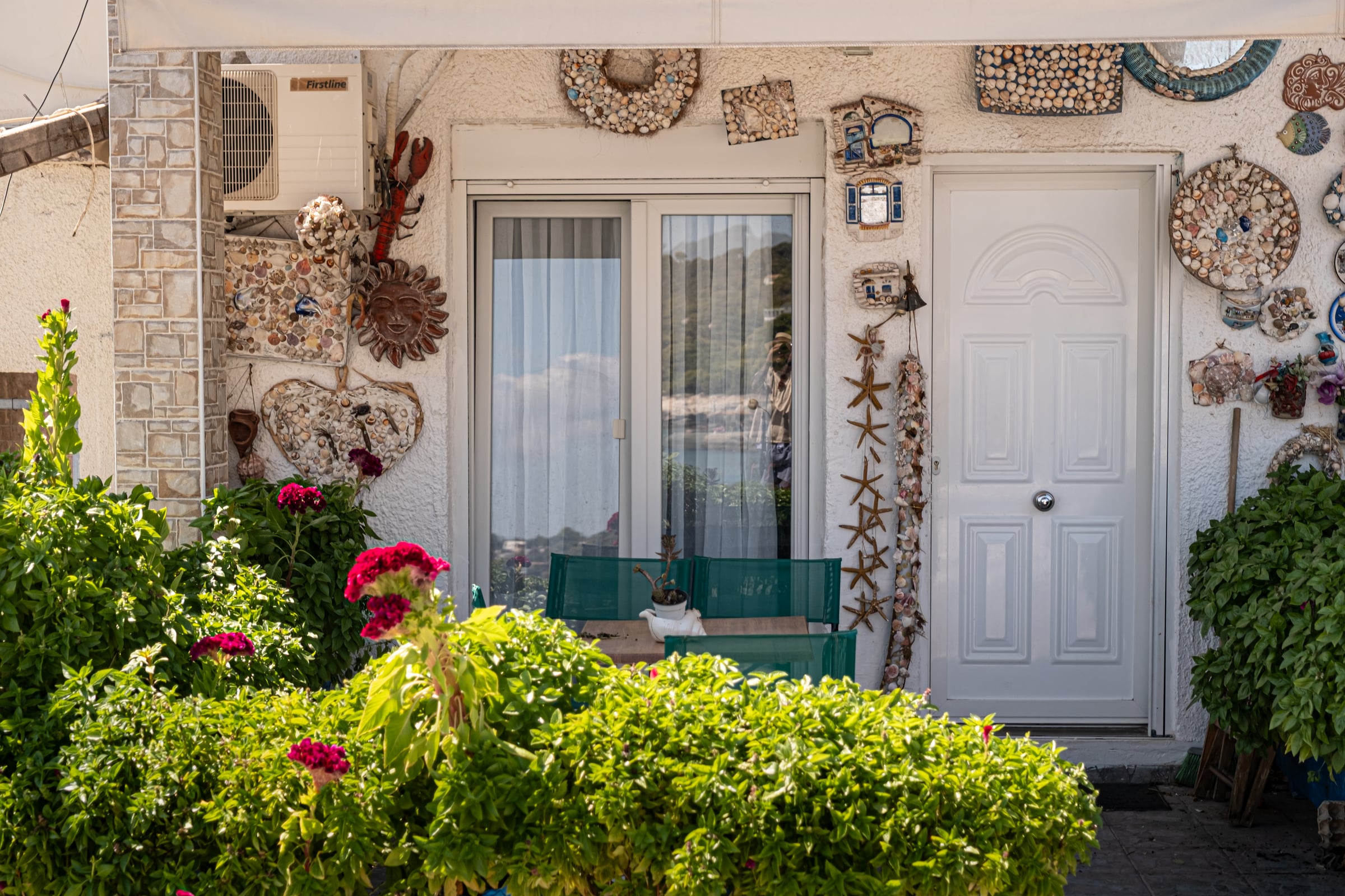 Greek house facade covered with shell art mosaics, starfish decorations and red flowers