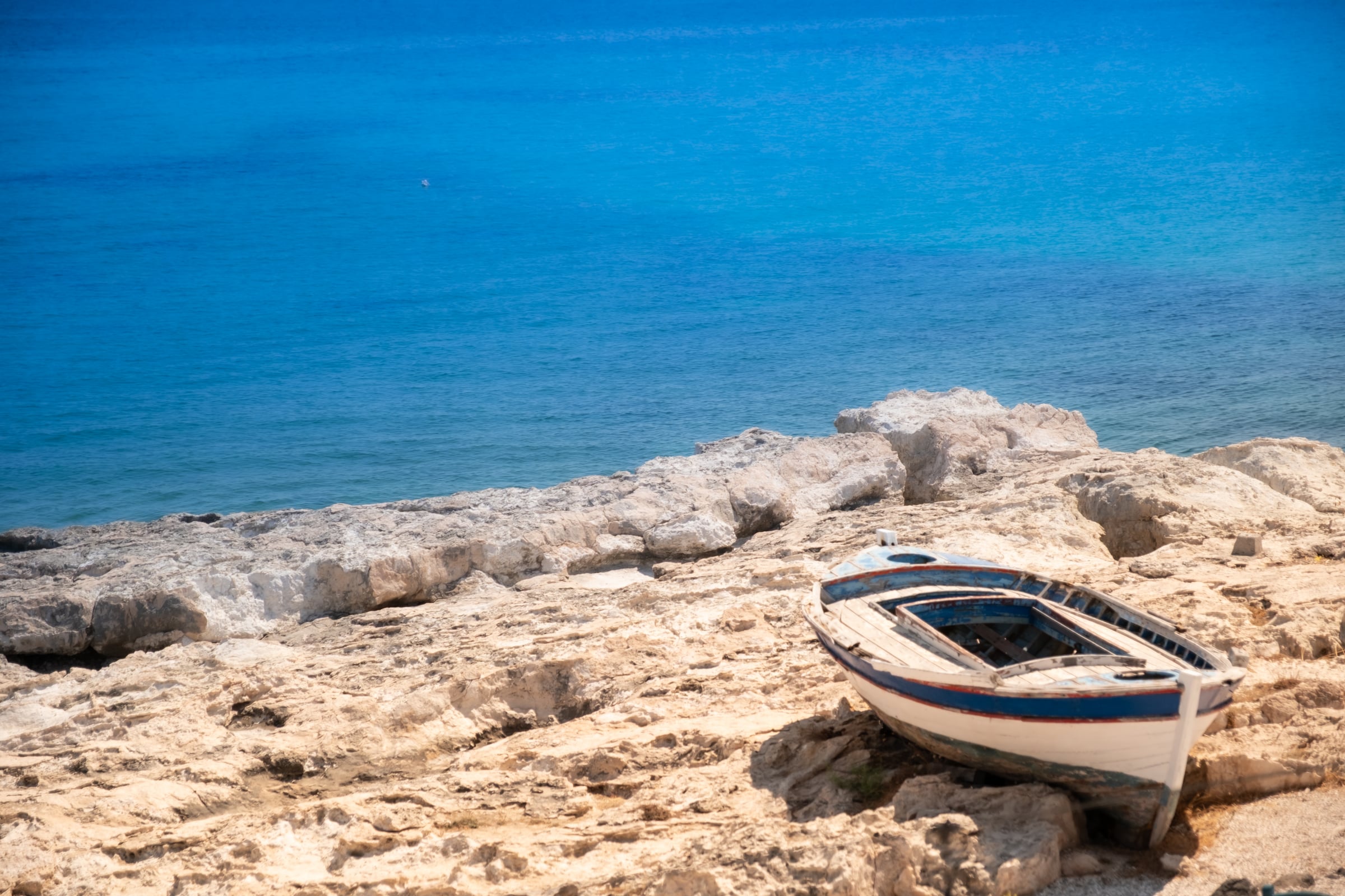 Old white-and-blue painted rowboat resting on white limestone rocks above turquoise sea