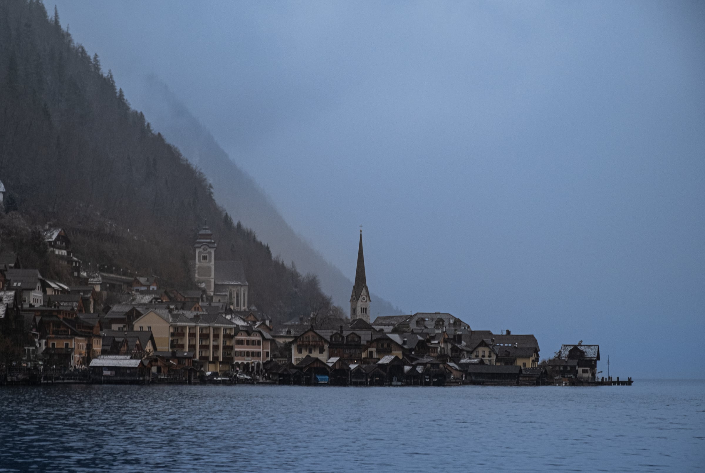 Hallstatt village with church spires and alpine houses on misty winter lake, mountains behind