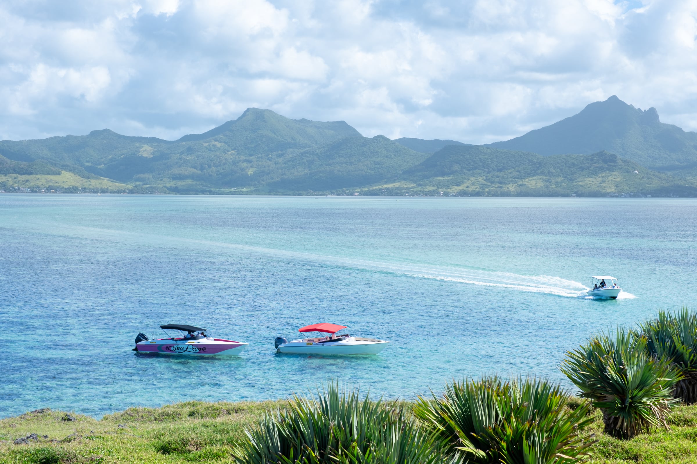 Mauritius lagoon with colorful motorboats and a speedboat leaving a wake, green mountains behind